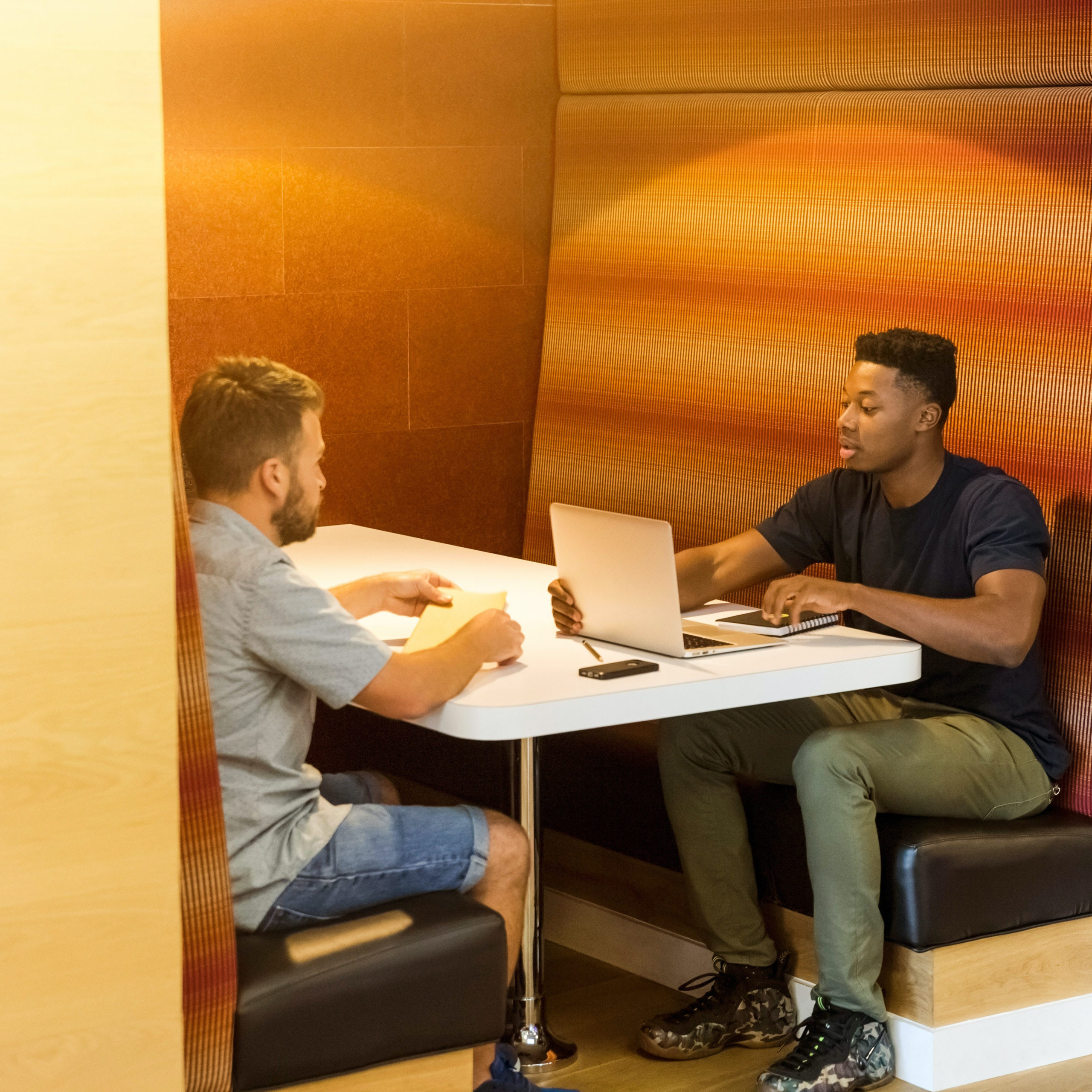 A black man and a white man sitting at a table in an office cafeteria.